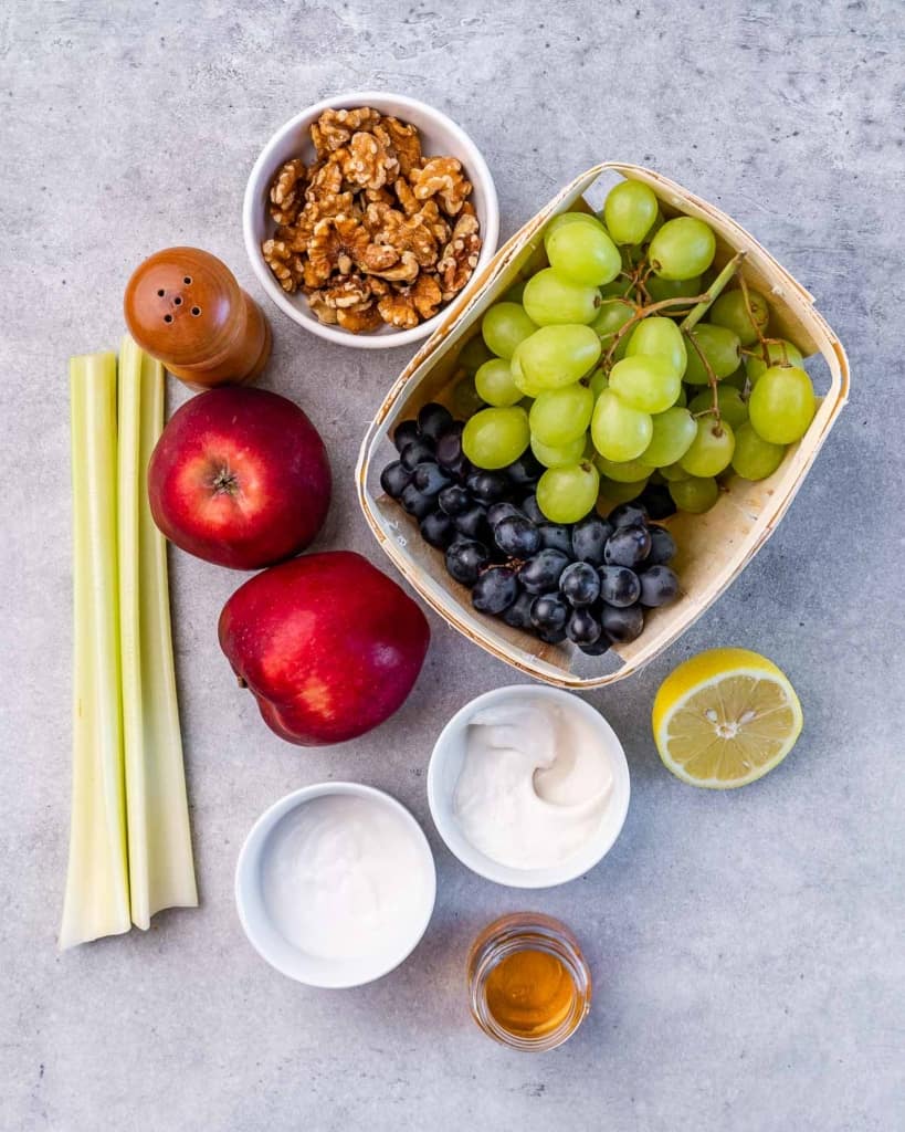 Grapes, apples, celery sticks, walnuts, honey, mayo and Greek yogurt divided into separate portions.