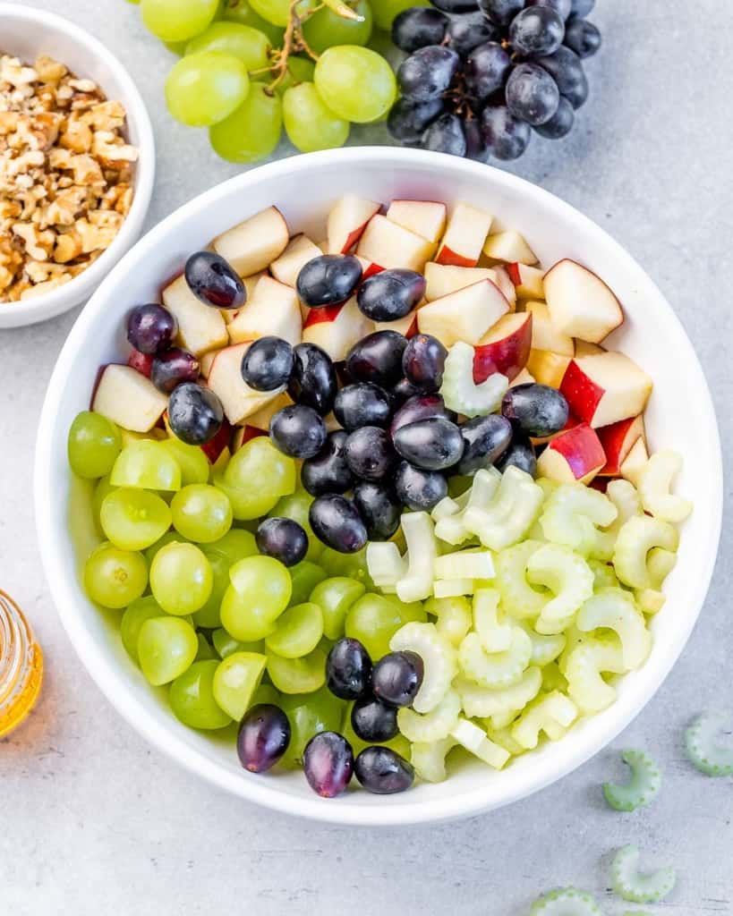 Grapes, celery, apples and walnuts in a white bowl.