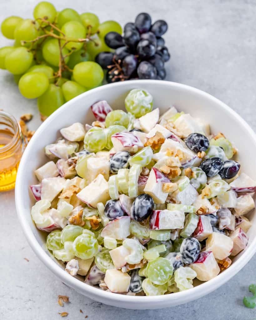 Waldorf salad recipe in a white bowl near a bunch of grapes.