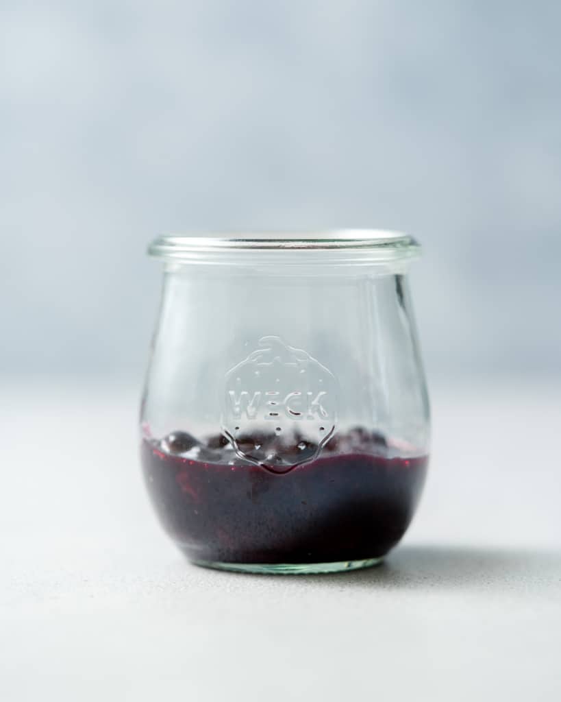 Adding blueberry sauce to a glass jar.