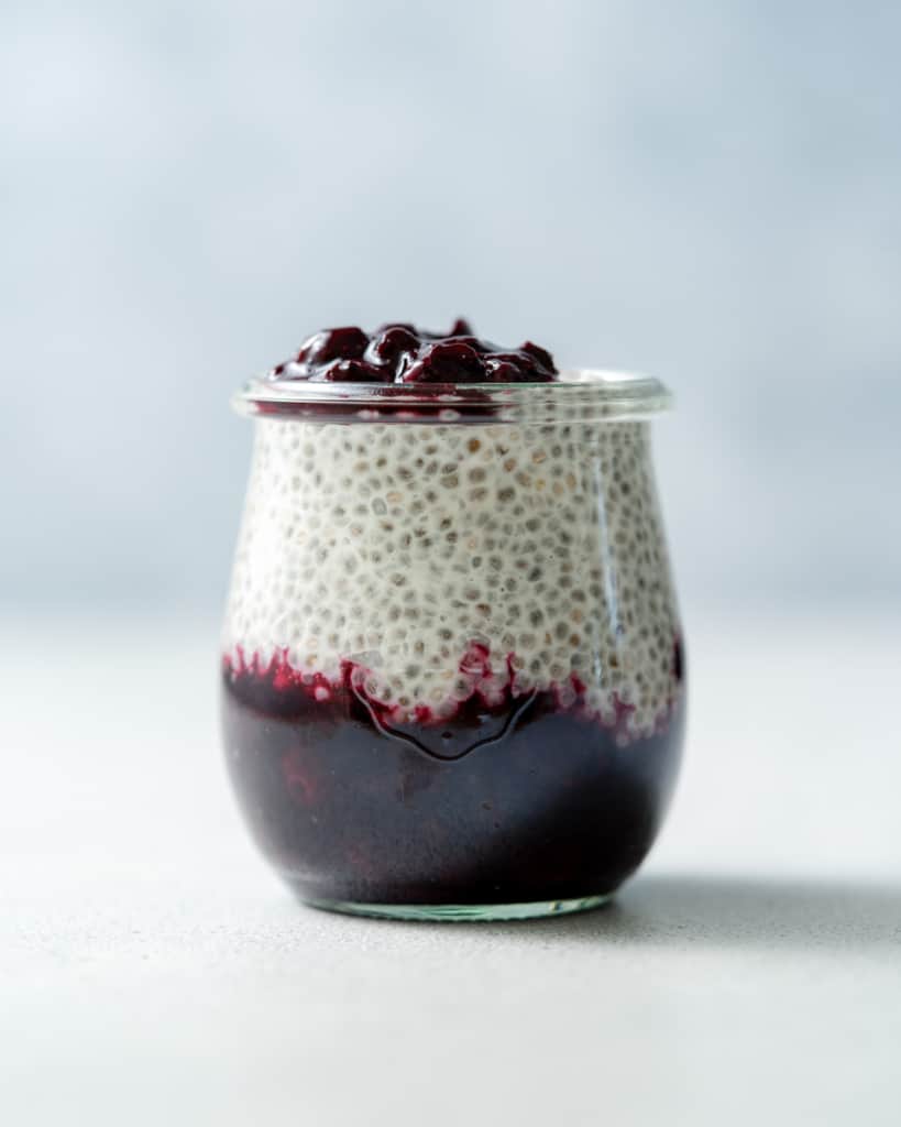 Glass jar with coconut chia pudding and blueberry sauce.