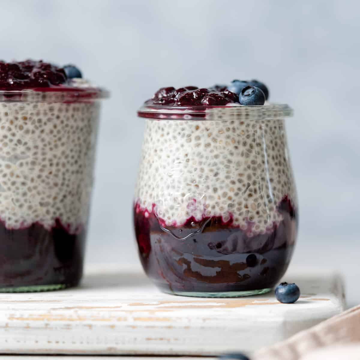 Side shot of a jar with blueberry jam at the bottom of the jar and chia pudding on the top layer topped with more blueberries.