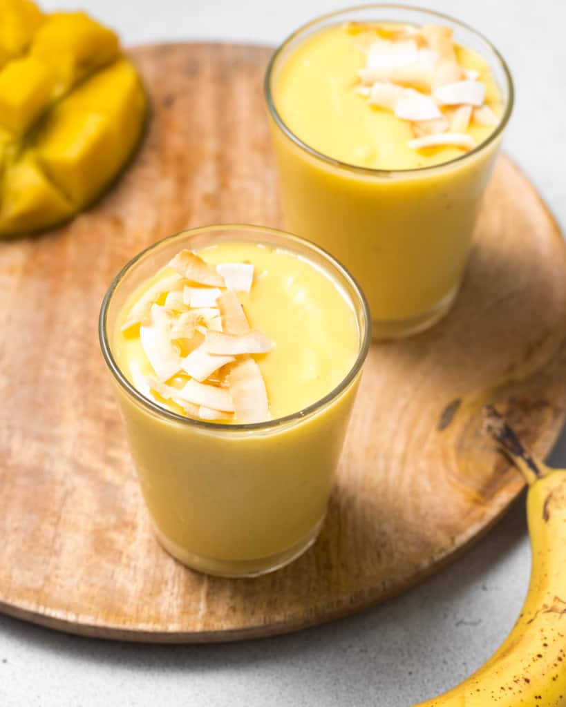 Side shot of mango smoothie in a cup topped with toasted coconut.