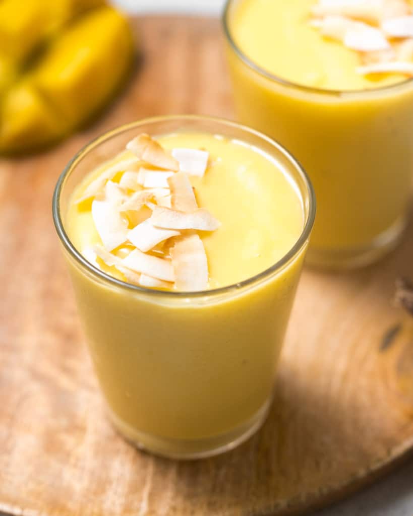 side shot of mango smoothie in a clear cup topped with toasted shaved coconut