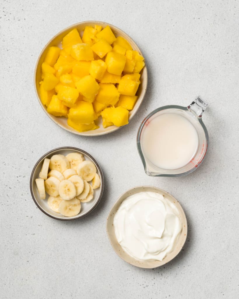 Chunks of mango, banana slices, milk and yogurt divided into separate bowls.