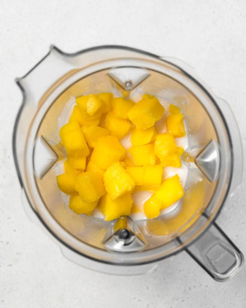 Adding chunks of mango into a blender.