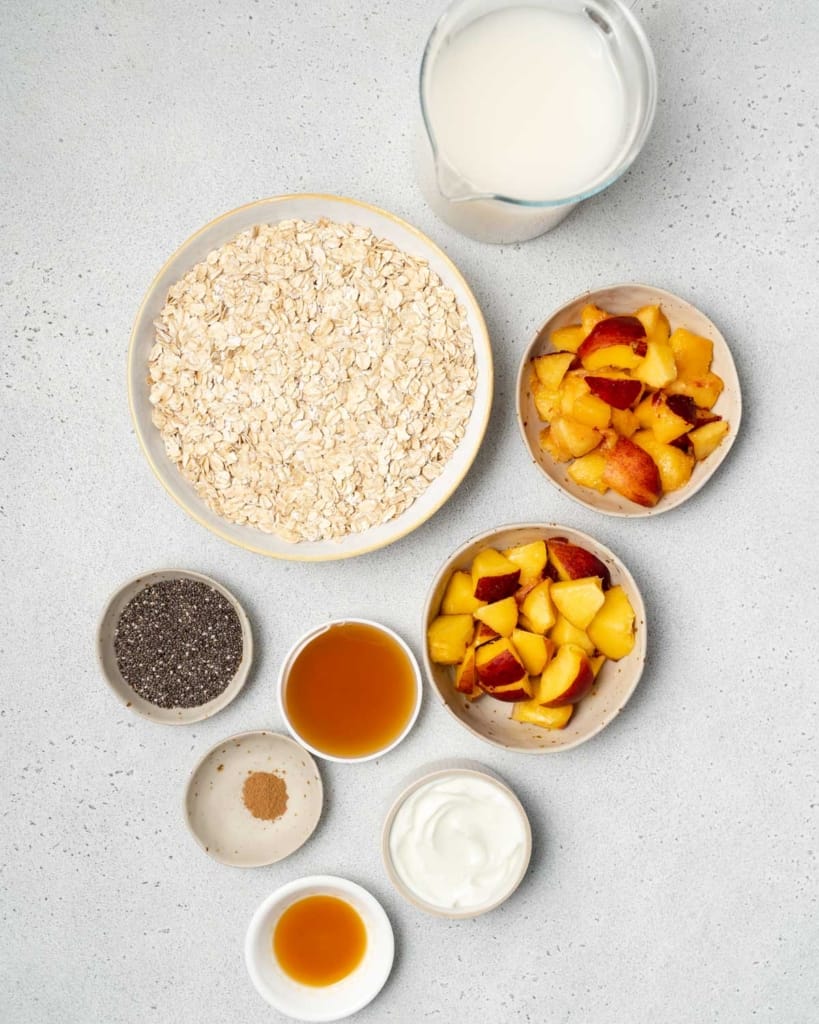 Oats, peaches, chia seeds, milk and other ingredients divided into small portions.