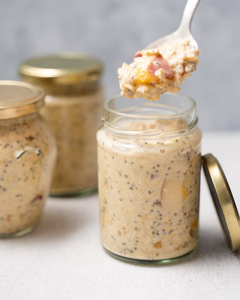Spooning out peach overnight oats from a jar.