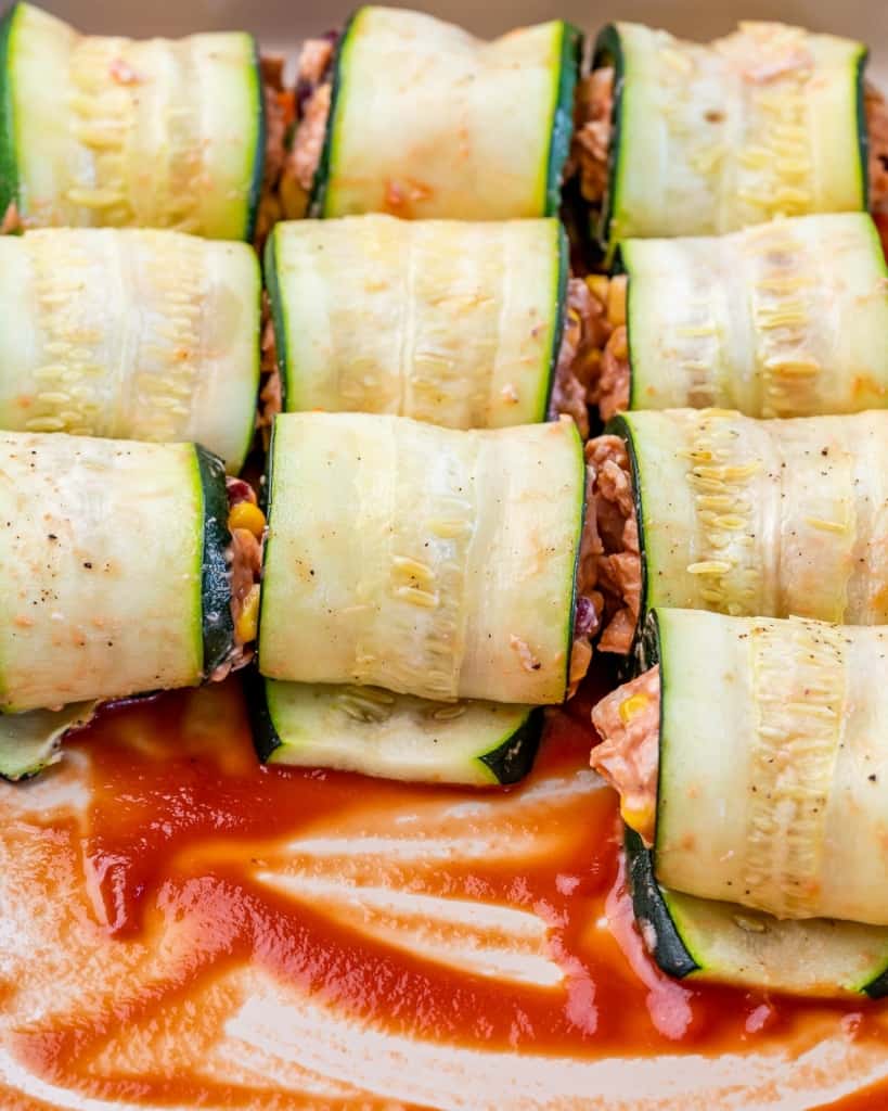 shredded chicken enchilada rolled with thinly sliced zucchini being assembled in a dish