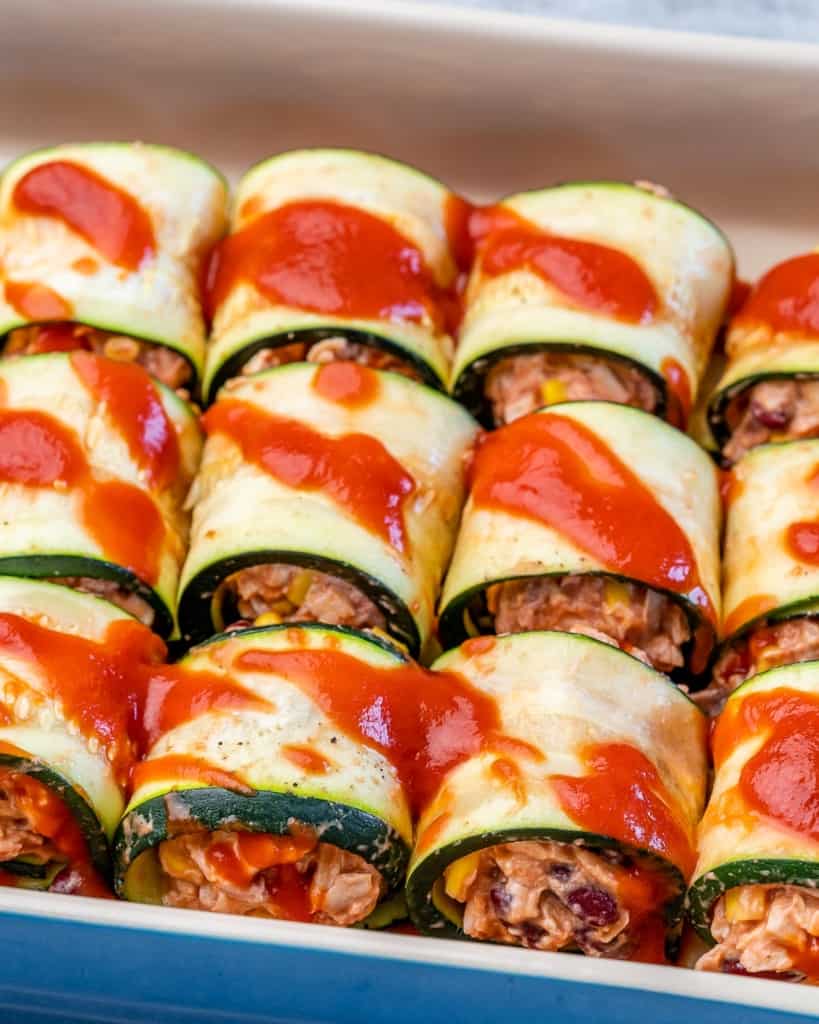 chicken enchilada rolls in a baking dish assembled next to each other  topped with red sauce 