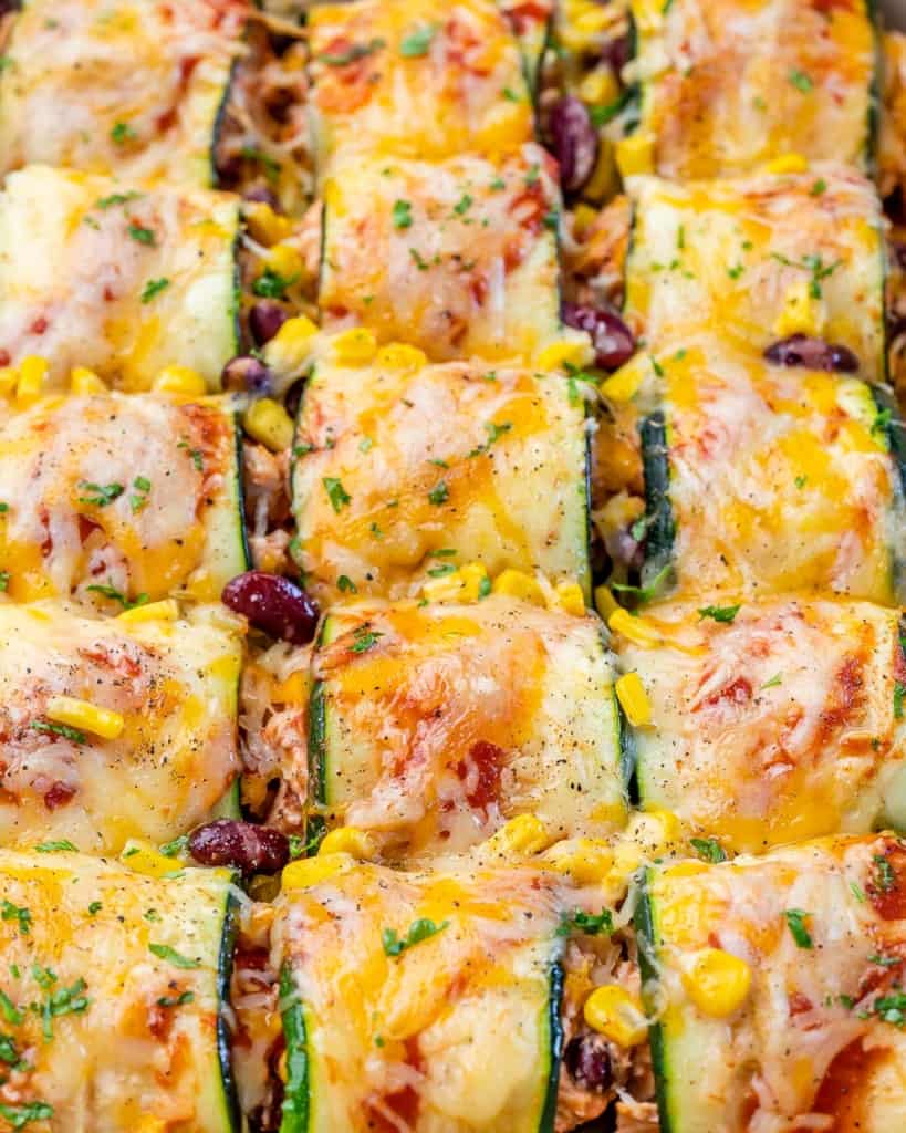 close up top view of chicken enchilada roll-ups with thinly sliced  zucchini topped with melted cheese in a dish