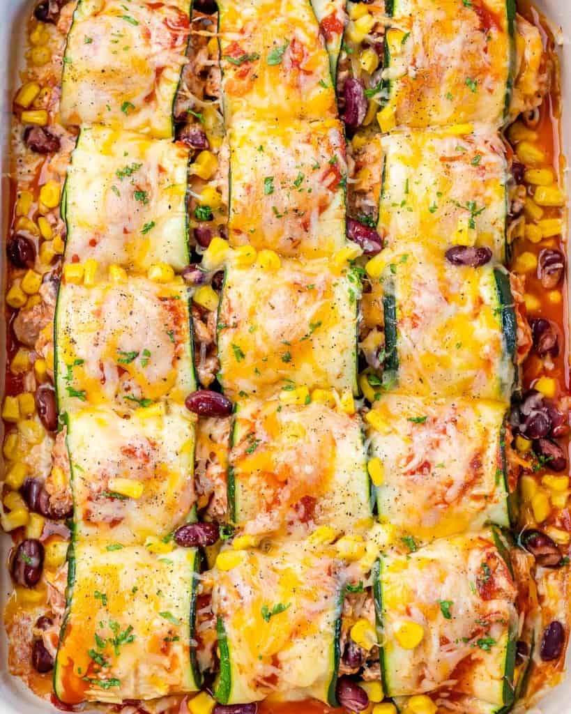 top view of chicken enchilada rolled with thinly sliced zucchini with a white dish with melted cheese on top
