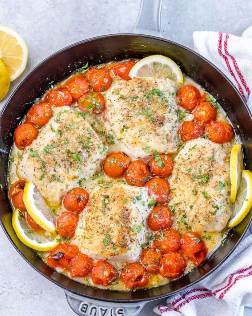 top view of a black skillet with baked lemon cods along with cherry tomatoes cod