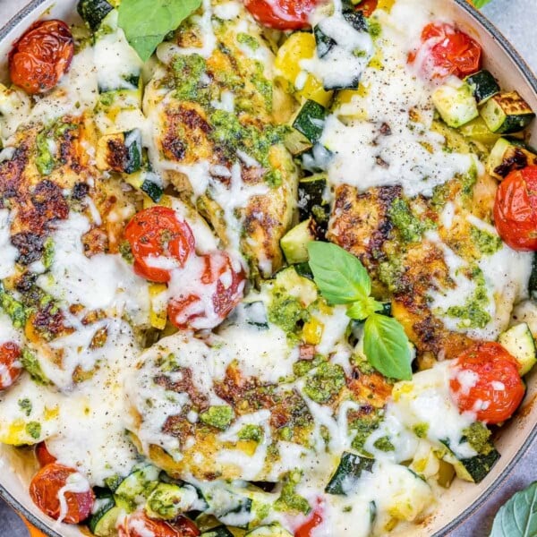 baked chicken breast over a skillet with pesto, veggies, and melted cheese