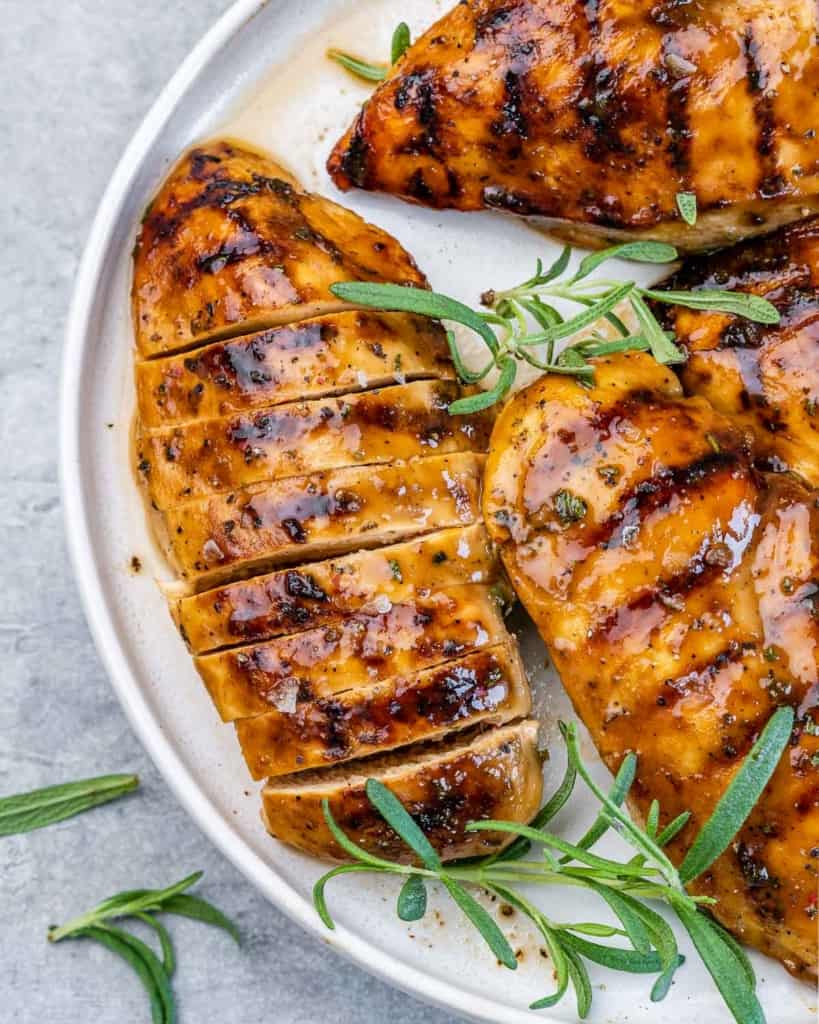 Sliced grilled chicken served on a plate with fresh rosemary.