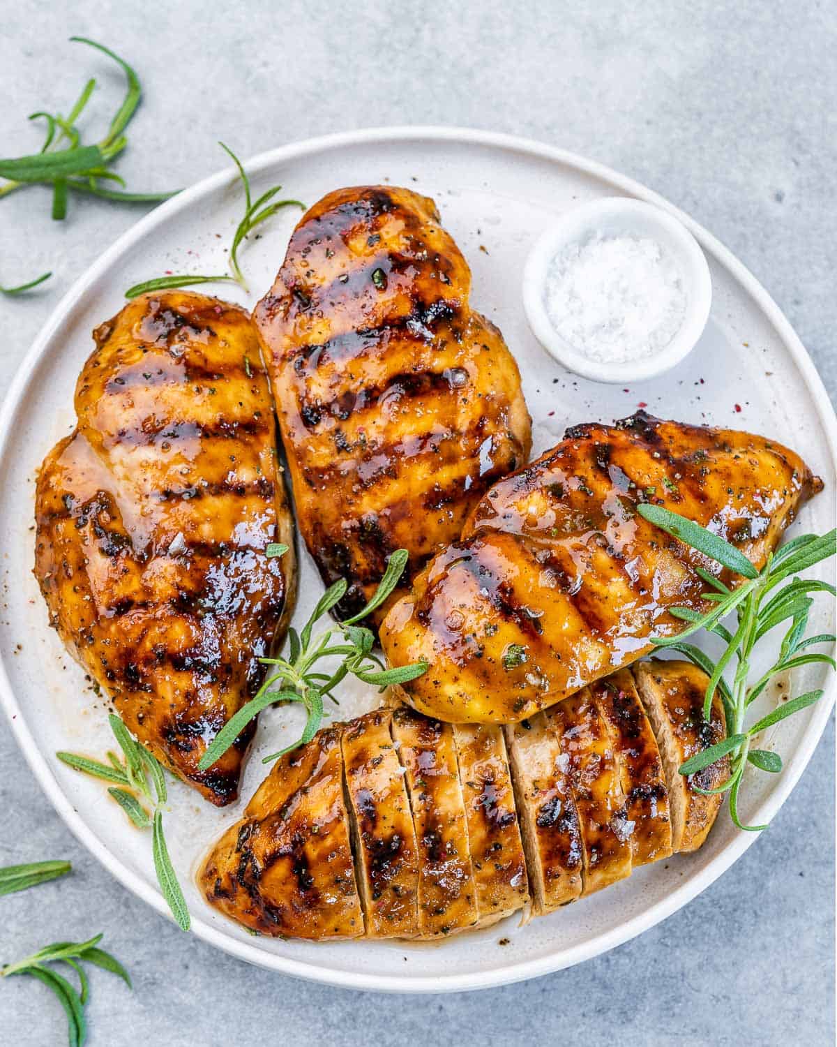Top view of 4 grilled chicken breasts over a white plate.