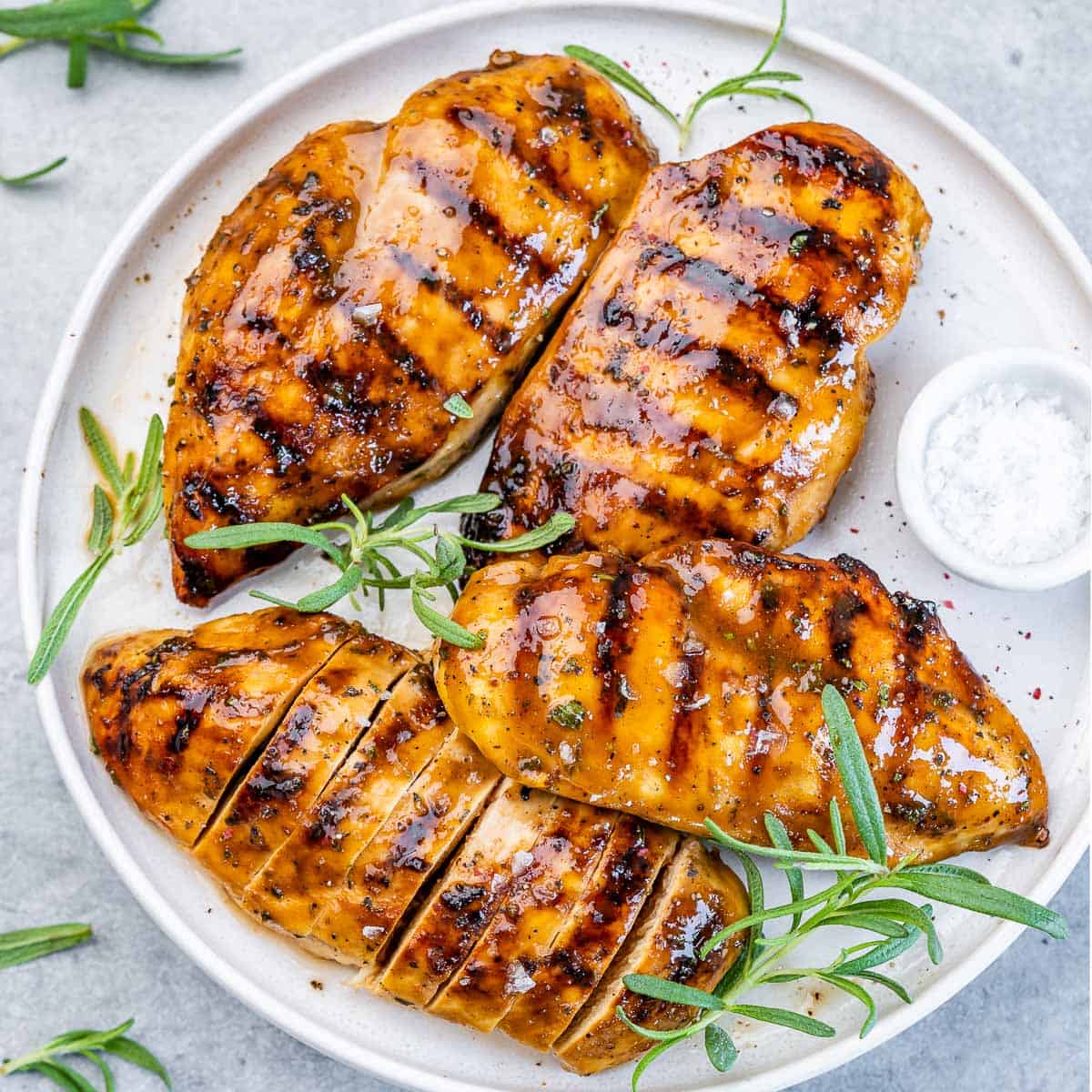 Top view of 4 grilled chicken breasts over a white plate.