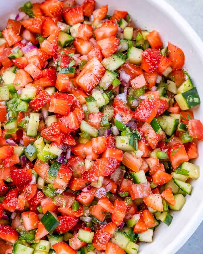 Diced strawberries, cucumbers, jalapeños and red onion in a large white bowl.