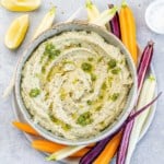 top view white bean dip in a bowl with veggie slices on the side to serve