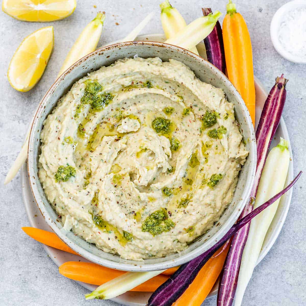top view white bean dip in a bowl with veggie slices on the side to serve