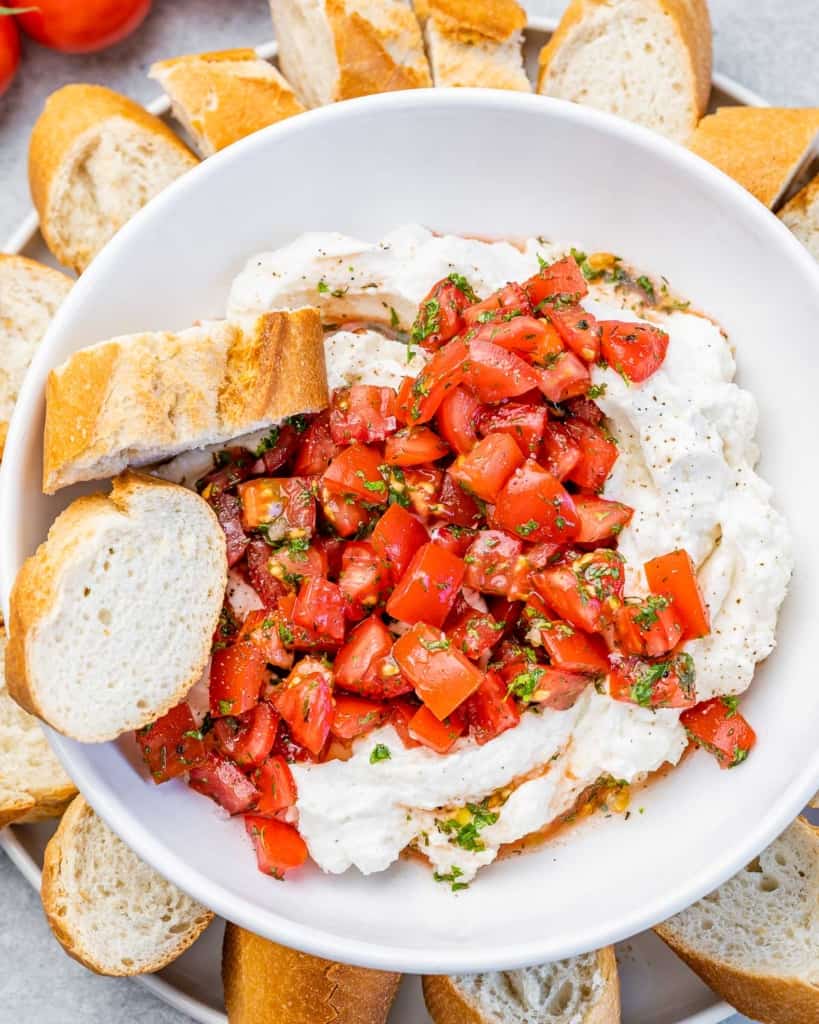 top view of plated whipped ricotta cheese topped with balsamic tomatoes with a side of 2 sliced baguette