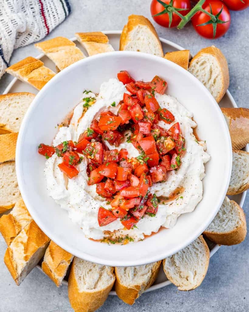 top view whipped ricotta cheese in a round white bowl, topped with a balsamic tomato blend.