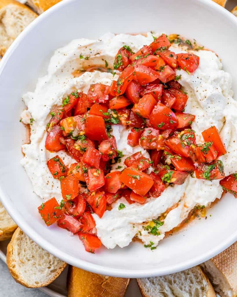 close up of whipped cheese topped with balsamic tomatoes in a round white bowl