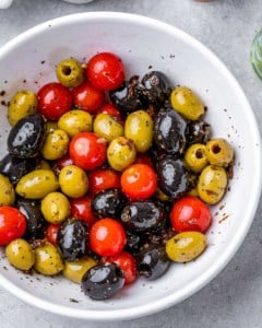 a bowl with olives and tomatoes tossed with oil and seasoning.
