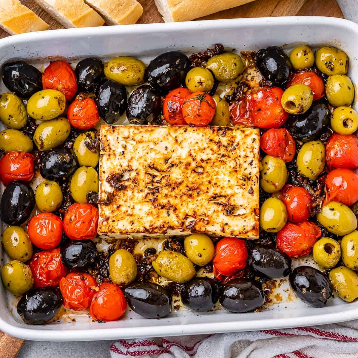 top view of white dish with baked feta cheese block and a mix of tomato and olives