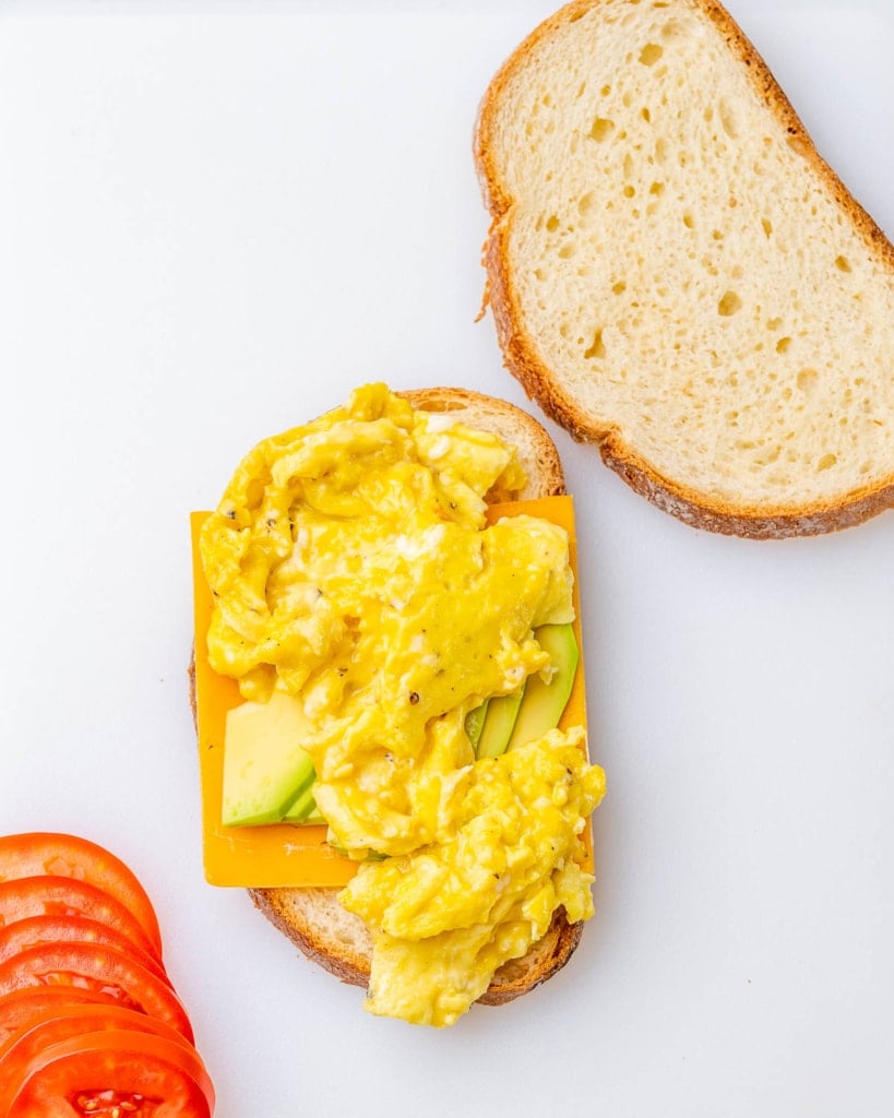Adding cheese, avocado and scrambled eggs to a slice of bread.