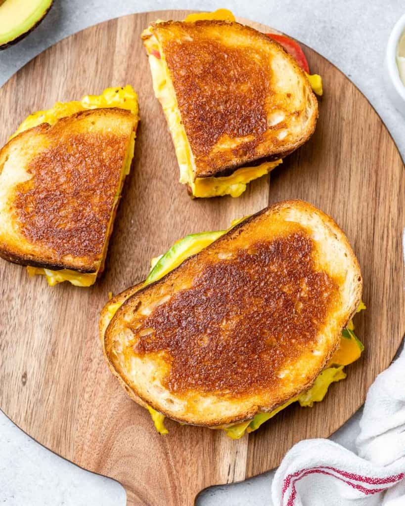 Toasted breakfast egg sandwich on a wooden cutting board.