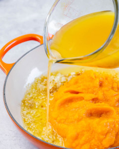 Pouring vegetable broth into pumpkin mixture.