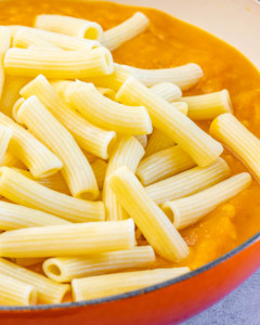 Adding pasta to pumpkin sauce in a pot.