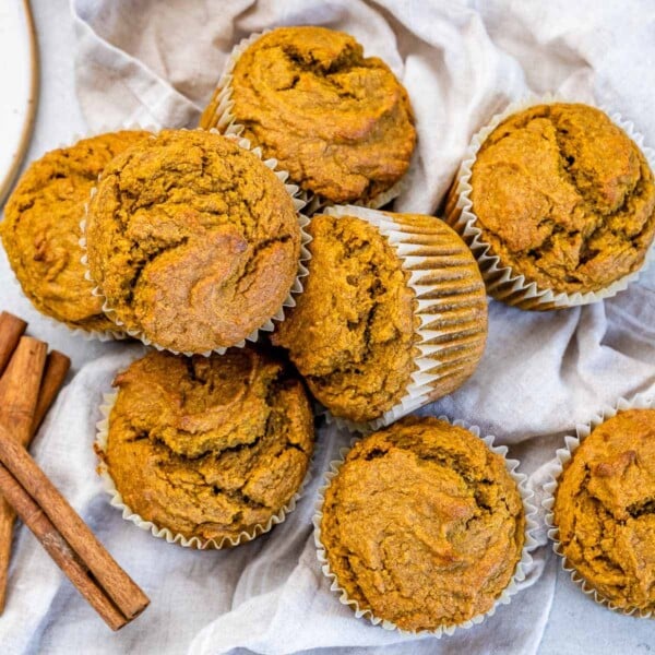 pumpkin muffins on a napkin with some cinnamon sticks on the left side by the muffins.