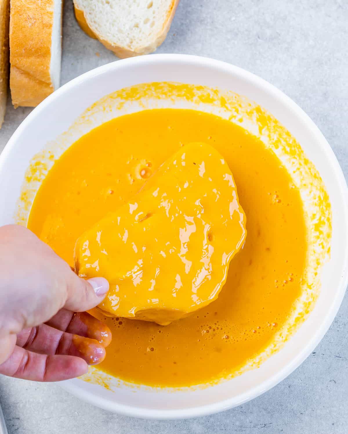 Dipping a slice of bread into an egg and pumpkin custard.