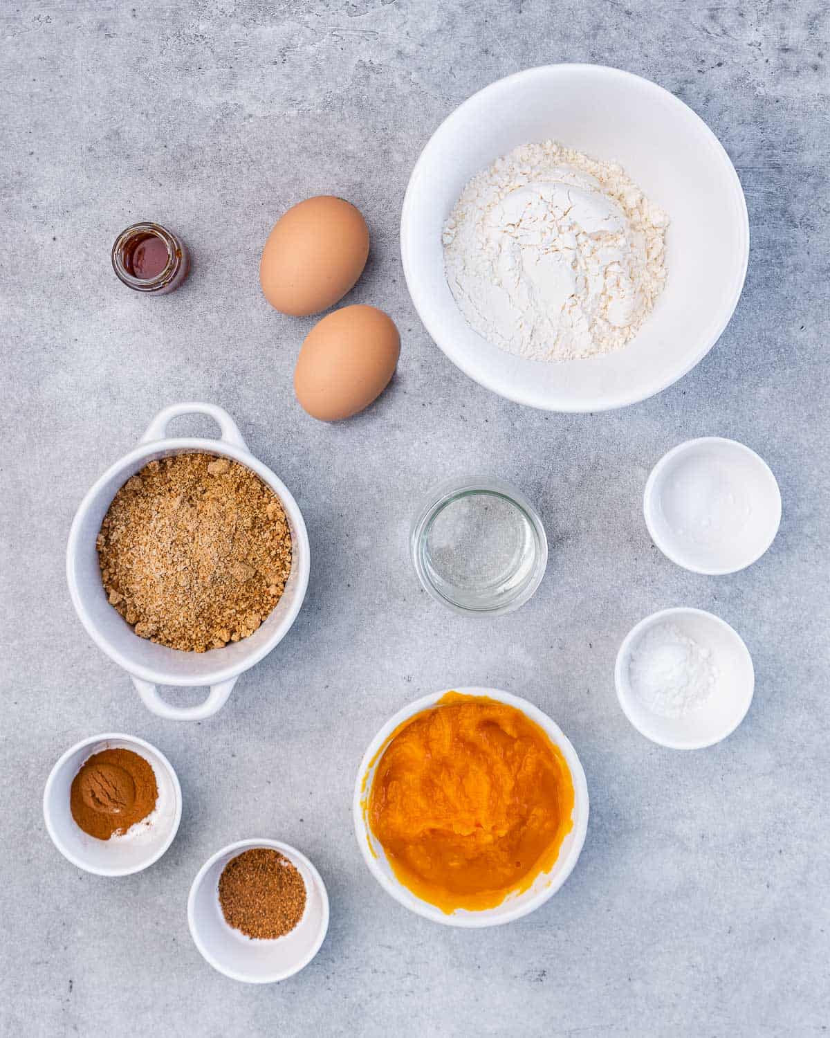 Pumpkin puree, flour, eggs, sugar, oil and spices divided into small bowls.