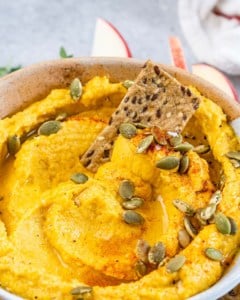 Closeup view of a seedy cracker dipped in pumpkin hummus.