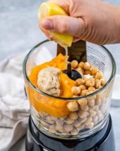 Squeezing lemon juice into a food processor with chickpeas and pumpkin puree.