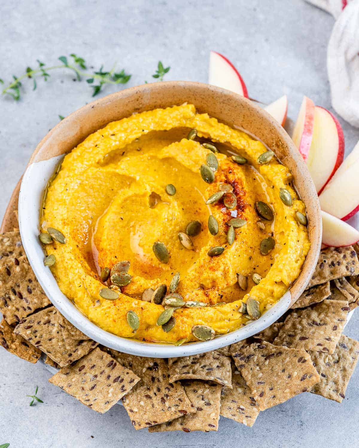 Pumpkin hummus topped with pumpkin seeds and served with crackers and apple slices.