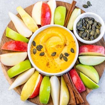 Top view of a white bowl with pumpkin pie fruit dip surrounded by apple slices.