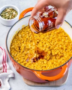 Adding maple syrup to cooked pumpkin oats in a pot.