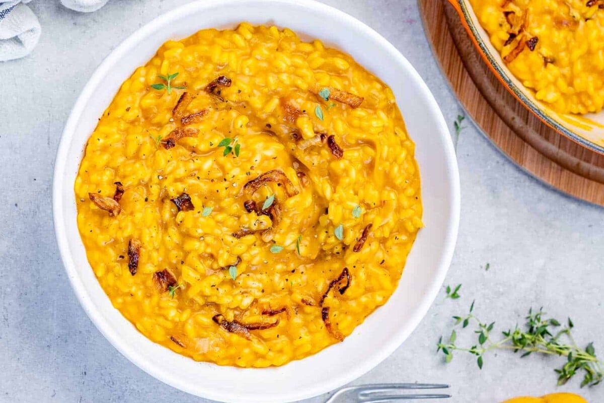 Pumpkin risotto in a white bowl garnished with fresh thyme and onions.