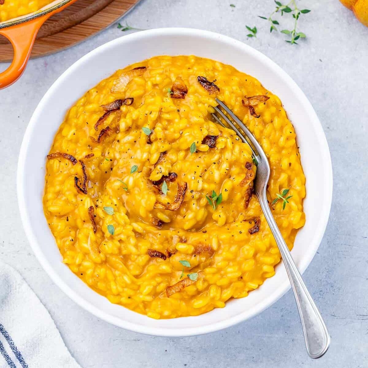 Pumpkin risotto served with a fork in a white bowl.