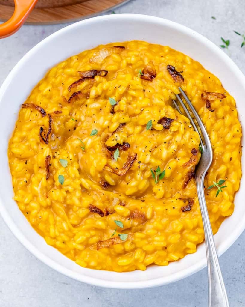 top view of pumpkin risotto in a round white bowl with spoon in bowl on the right side