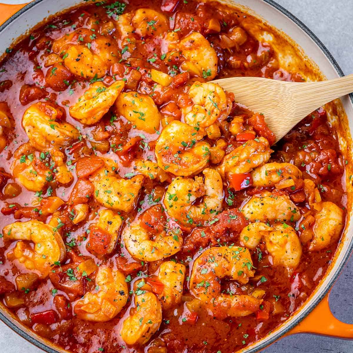 top view creole shrimp sautee in a red tomato sauce with wooden spoon in skillet
