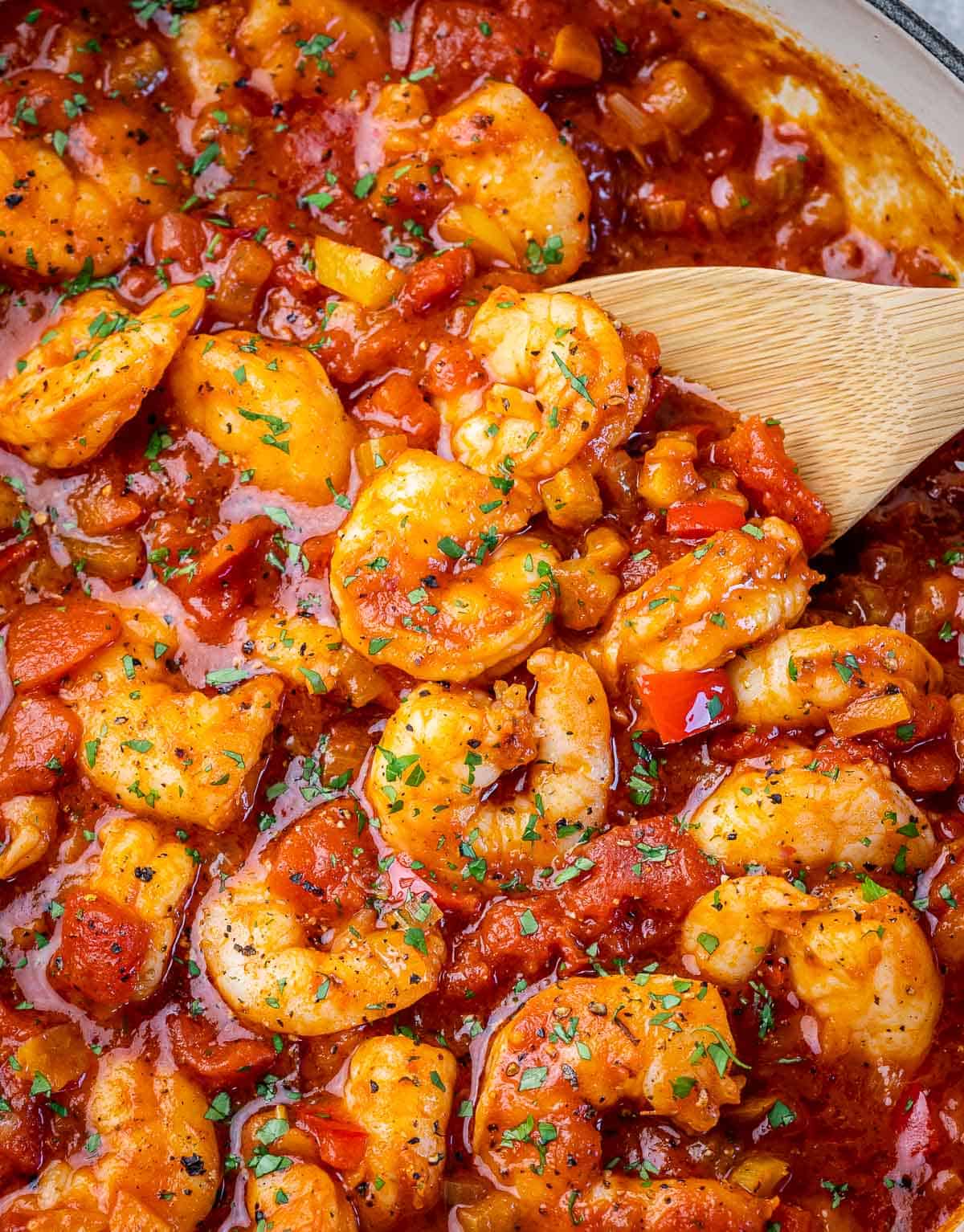 Using a wooden spoon to serve shrimp in a tomato based sauce.