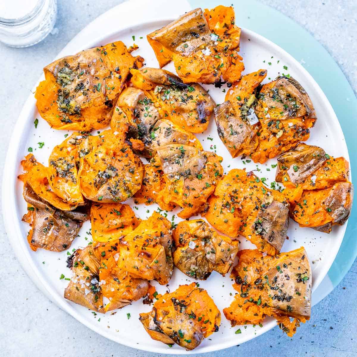 Top view baked smashed sweet potatoes on a round white plate.
