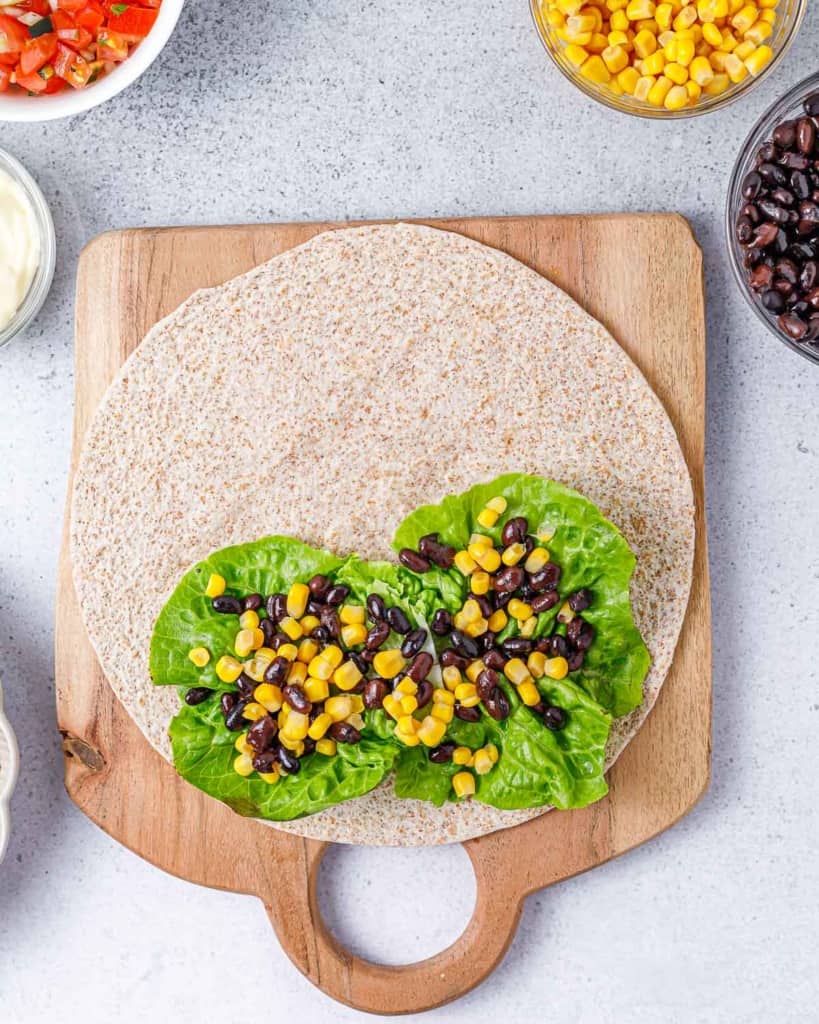 corn added over beans and lettuce on a tortilla wrap