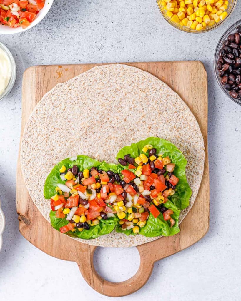 pico de galo added over corn beans and lettuce on a tortilla wrap