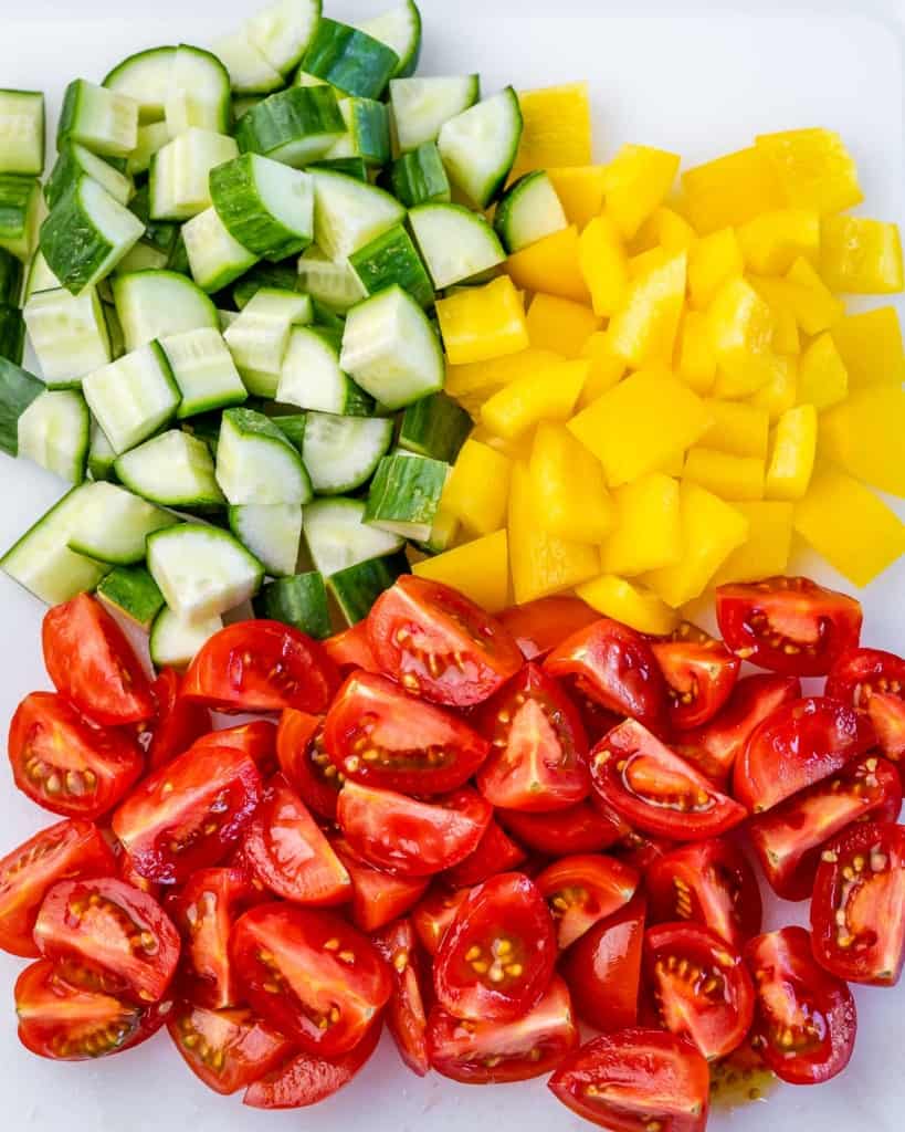 chopped cucumber, bell pepper, and tomatoes on a cutting board